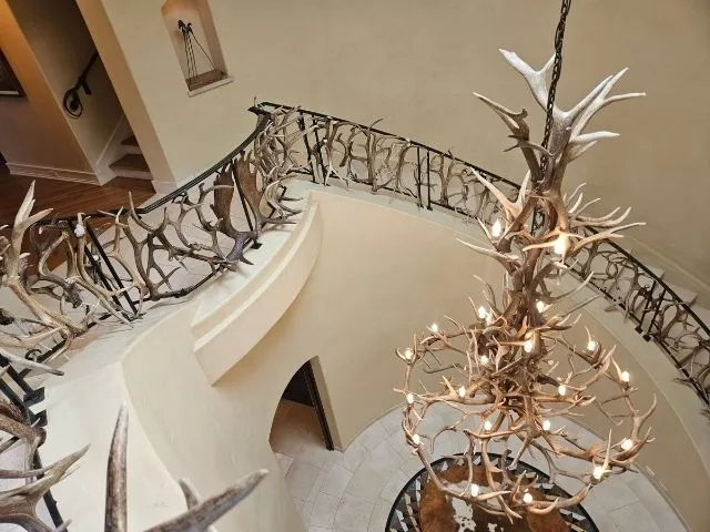 A Mt. Elbert antler chandelier hanging in a grand spiral staircase with antler railing in Colorado