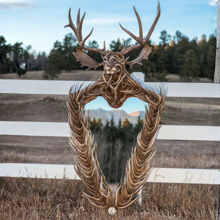 A mirror framed with antlers with deer bust antler sculpture resting at the top